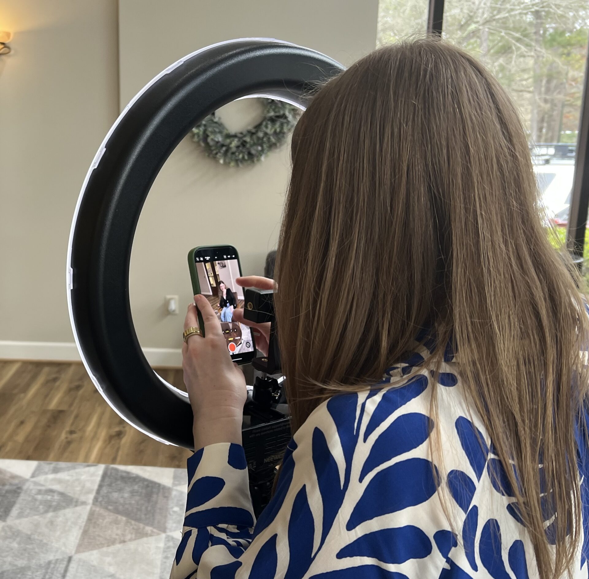 Behind the scenes of Christina Colantonio capturing content on an iphone with a ring light in front of her in an office setting.