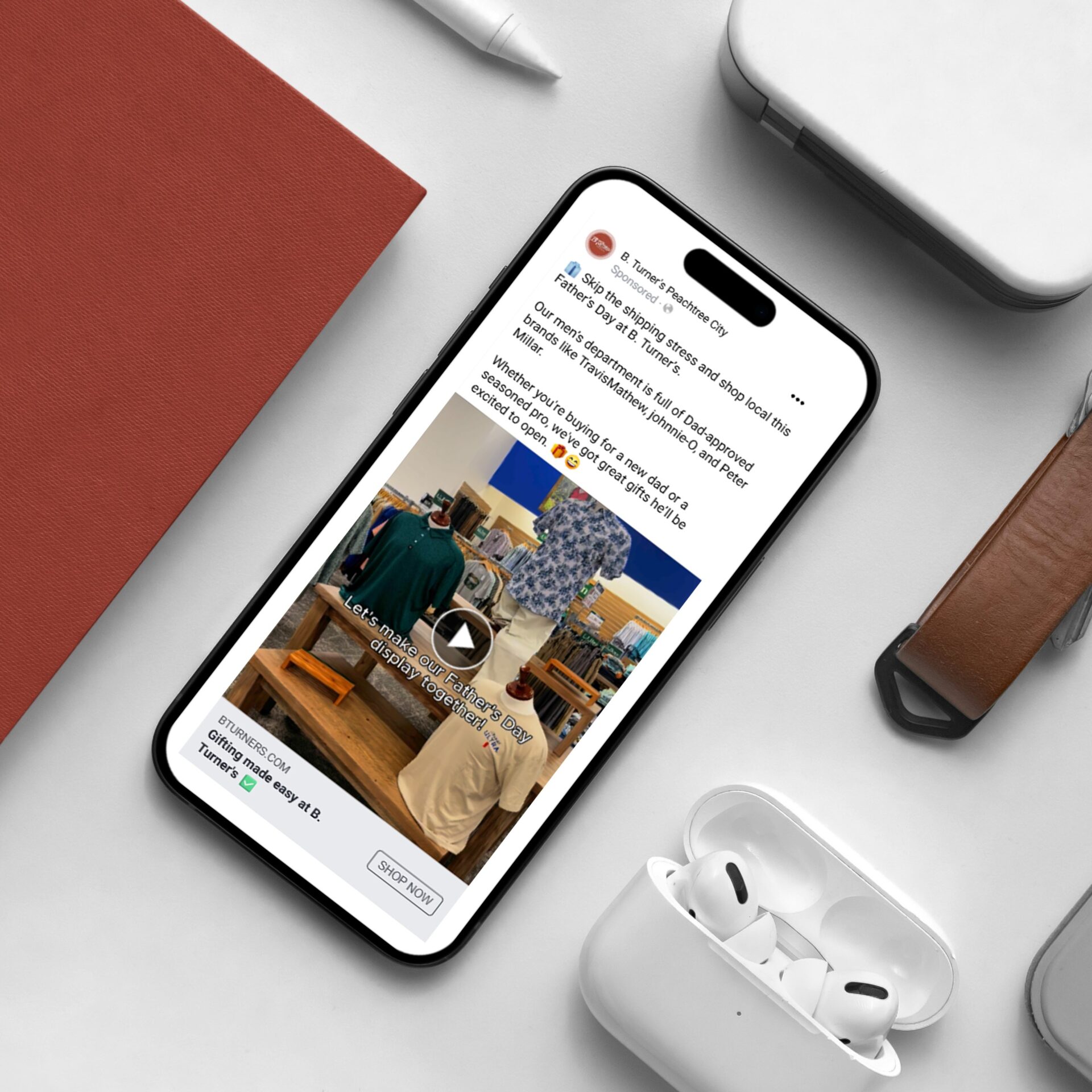 Flatlay image of an iphone displaying a Father's Day ad for B.Turner's Peachtree City. Beside it are a pair of airpods.