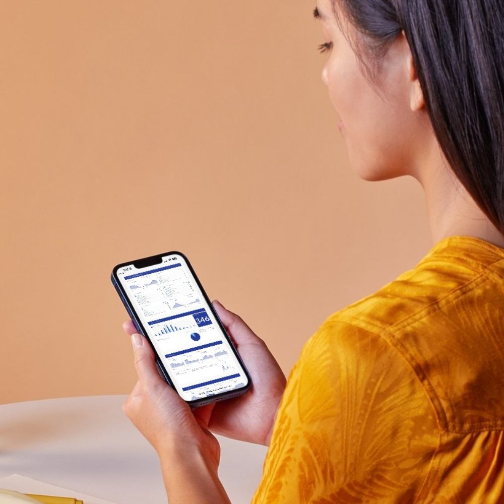 A woman looking at a smartphone displaying a custom marketing analytics dashboard by Country Fried Creative.