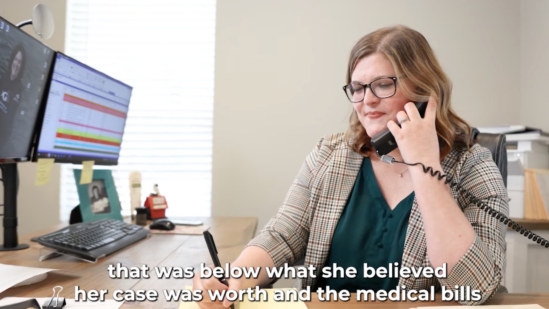 A woman on the phone at her desk in an office setting.